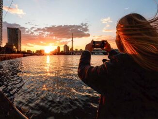 東京湾で夕焼けをスマホ撮影する女性