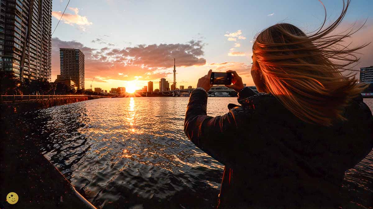 東京湾で夕焼けをスマホ撮影する女性